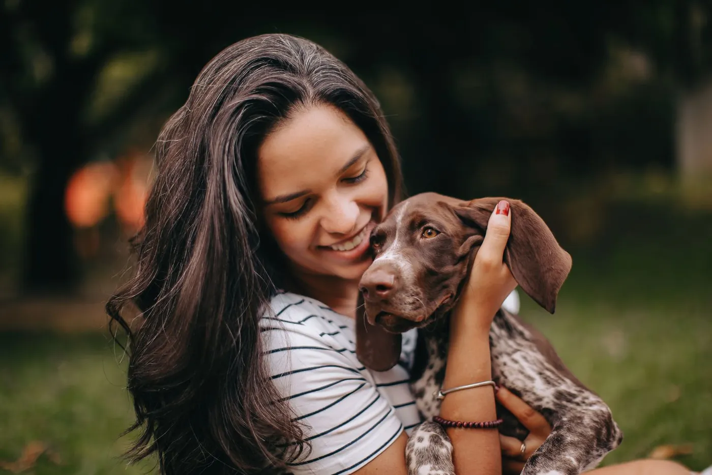 Une femme serre contre elle un chien braque brun, dehors.