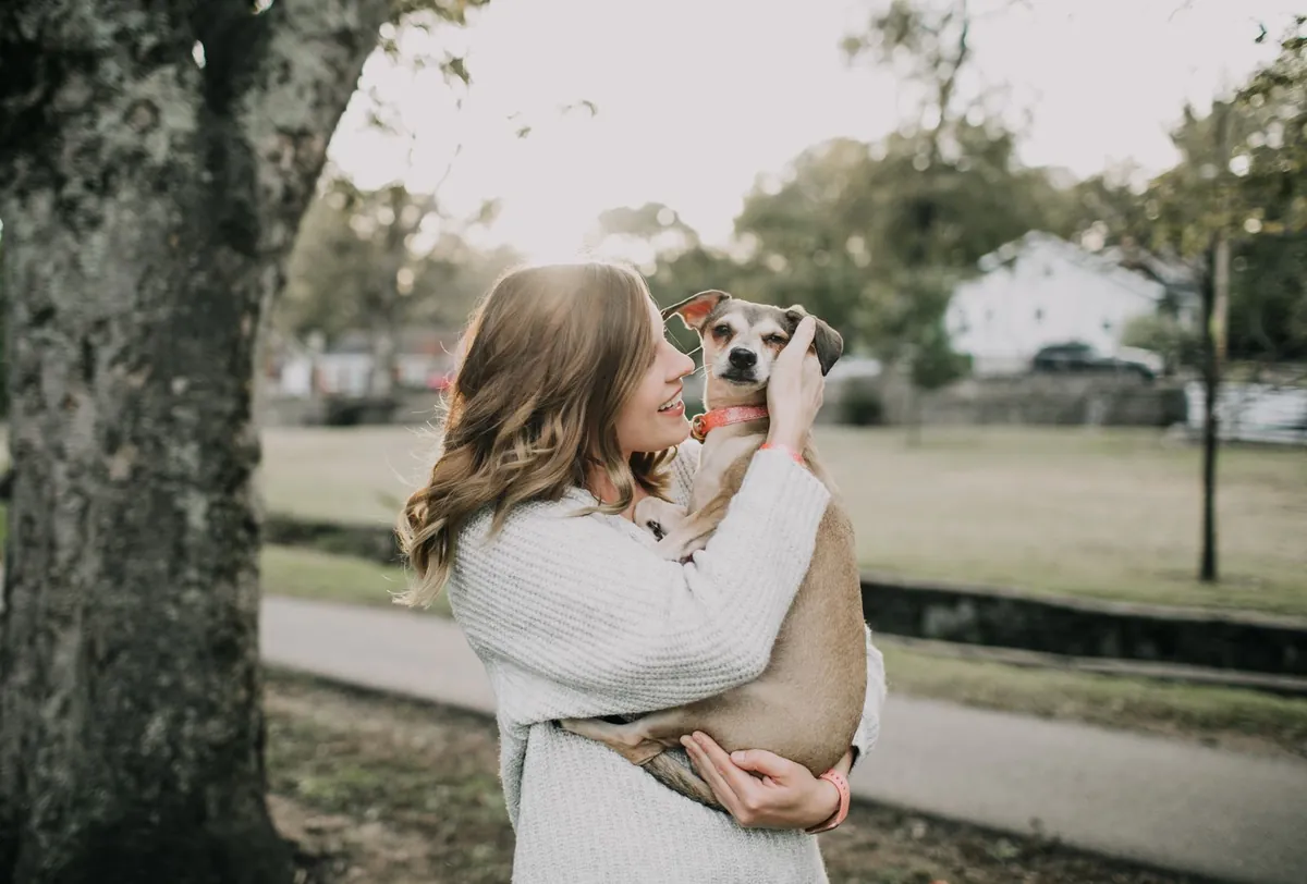 Une femme porte un jack russell dans ses bras, dans un parc.
